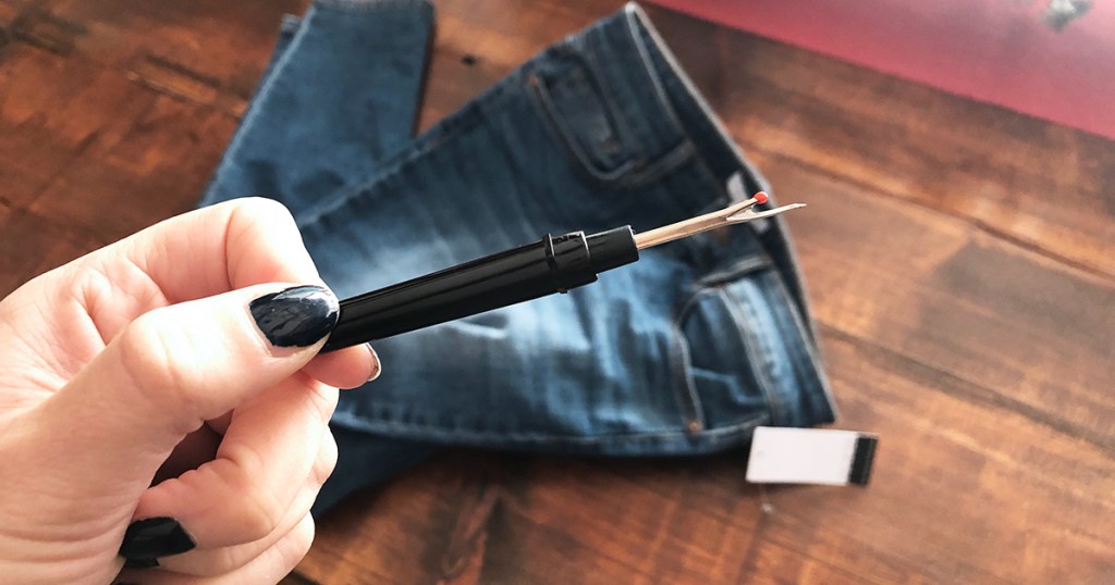 released hem denim diy &mdash; holding up seam ripper tool in front of denim jeans