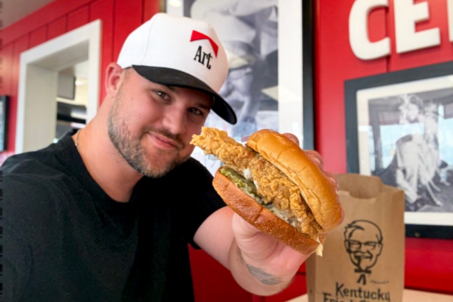 man holding chicken sandwich in restaraunt