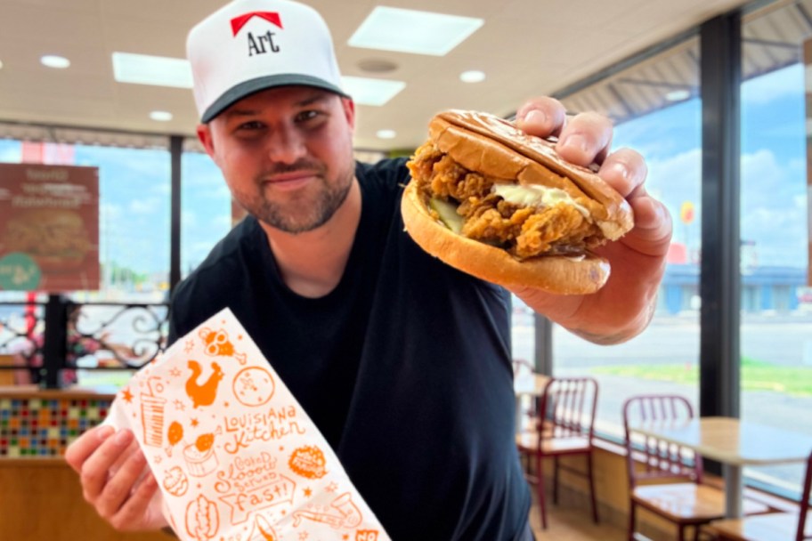 man holding popeyes chicken sandwich and bag in restaurant