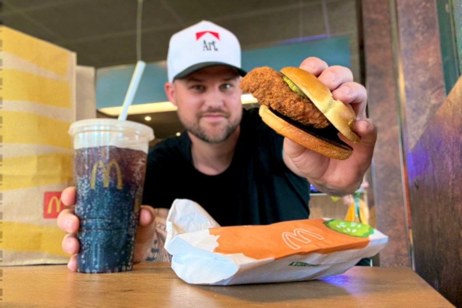 man holding chicken sandwich and drink outside restaraunt