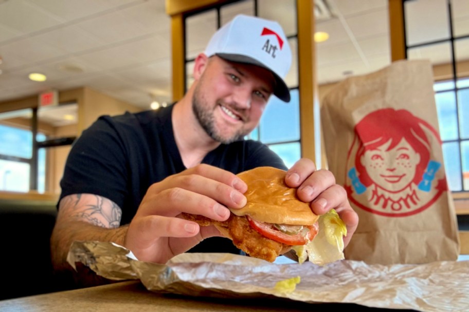 man holding wendys chicken sandwich next to wendys bag