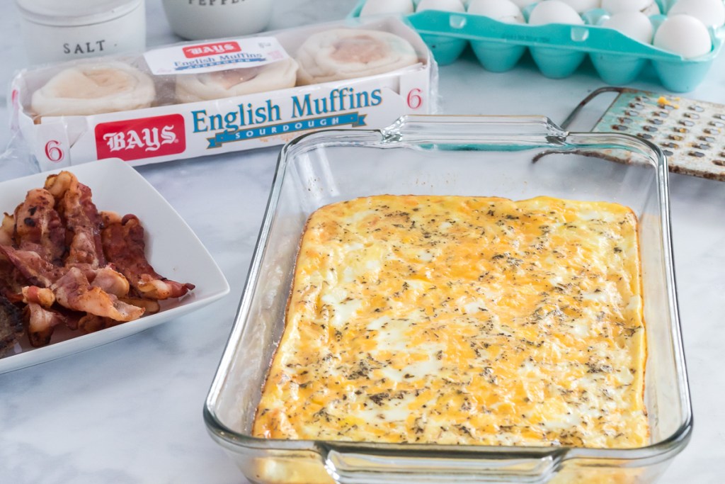 eggs cooked in a 9x13 pan with a plate of bacon and English muffins