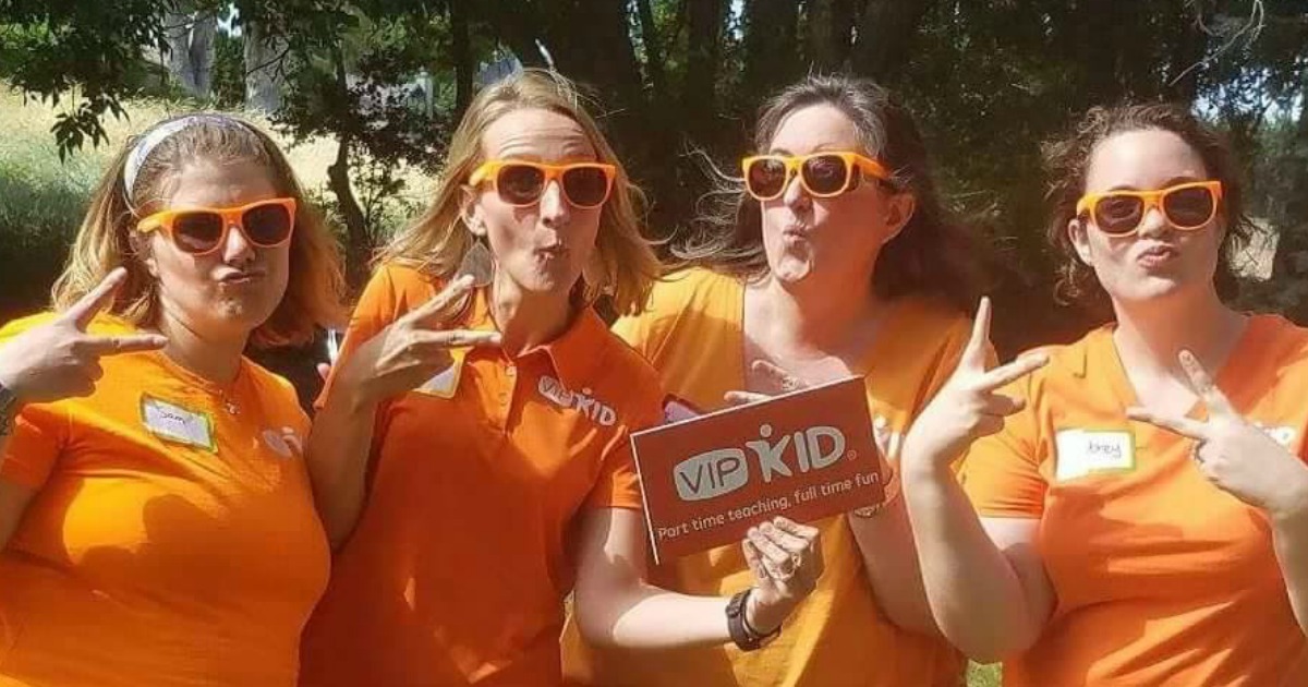 four women standing in orange shirts holding a sign in the park