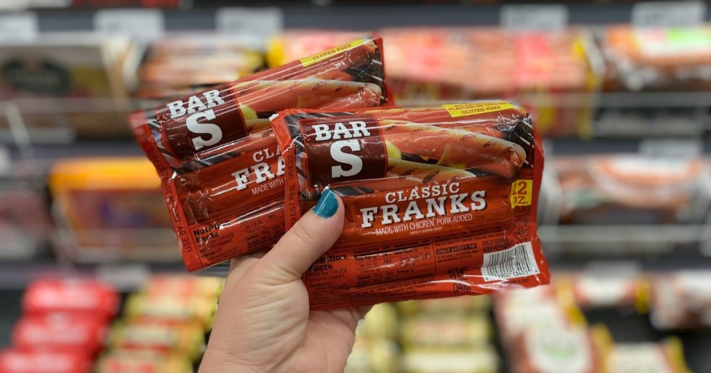 person holding 2 packages of Bar-S Franks in front of store cooler