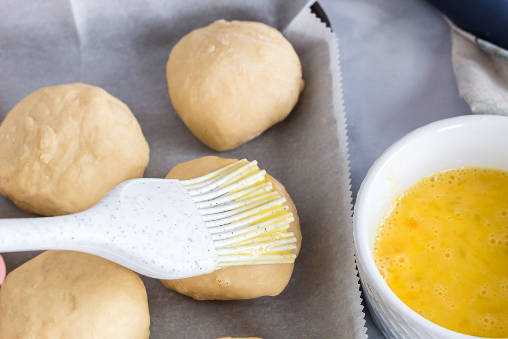 brushing egg wash onto dinner rolls
