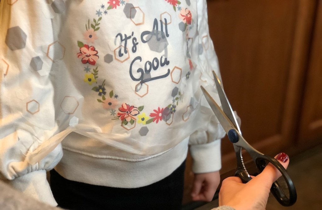 scissors cutting plastic on white sweatshirt
