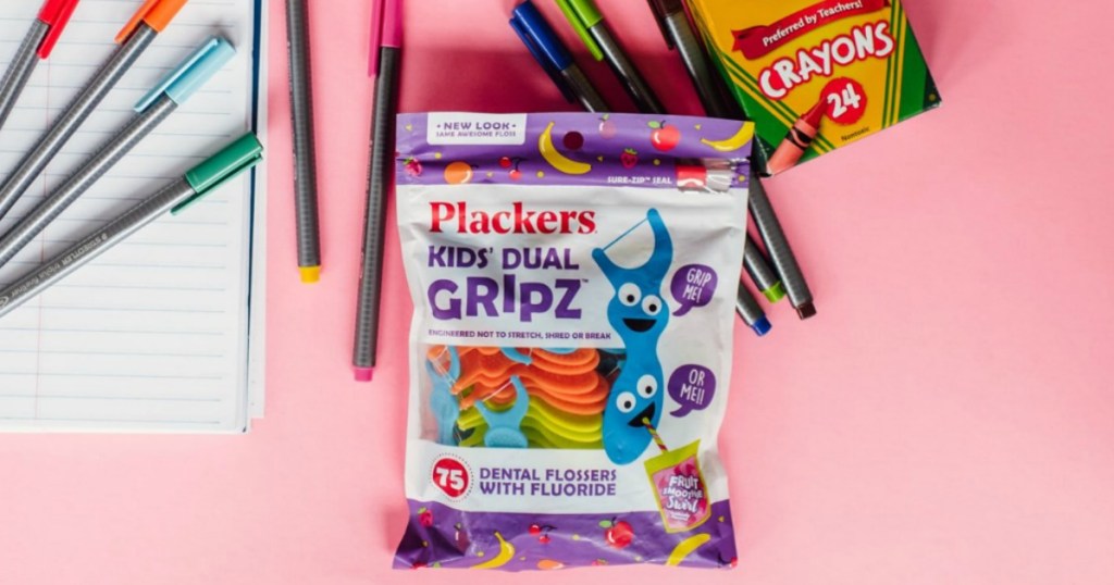 Plackers kids floss picks bag surrounded by crayons and markers on a pink background