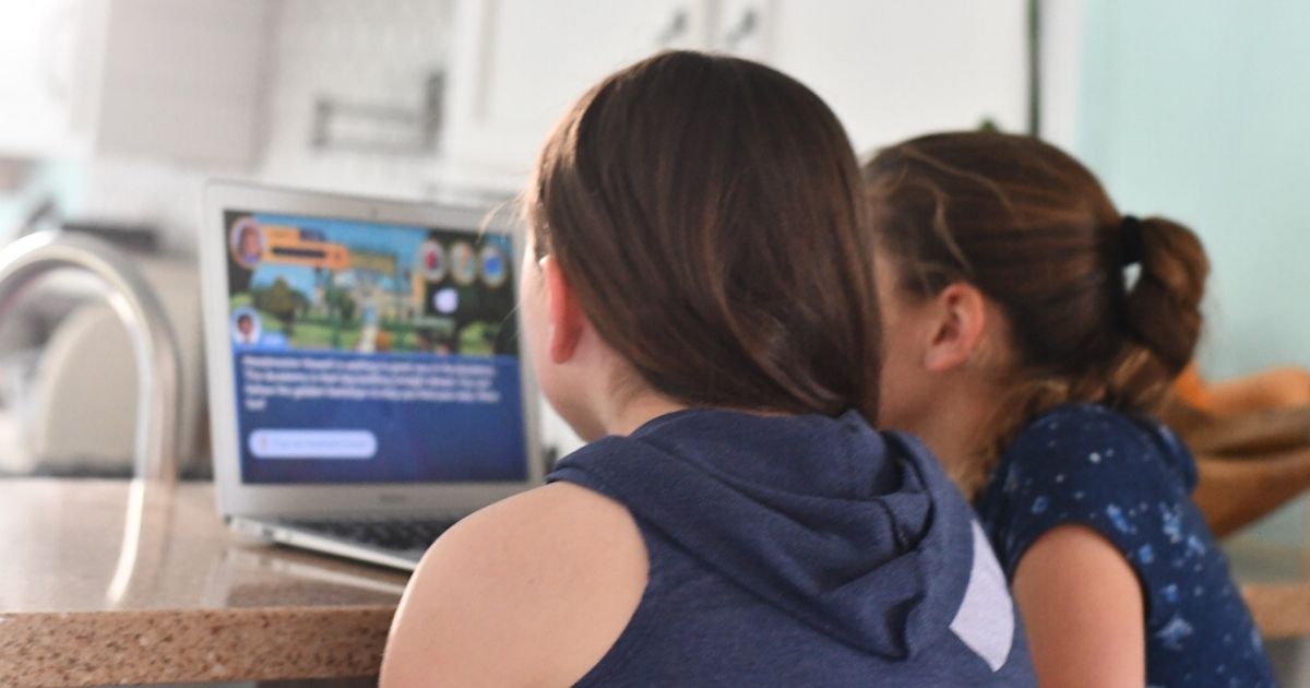 two girls on computer playing a game with their backs to the camera because they are getting free internet for students in 2023