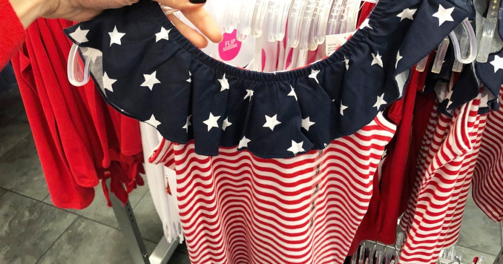 person holding up red and white striped dress with navy blue with white stars ruffle neck dress on hanger