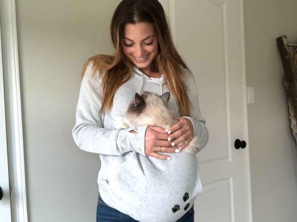 woman wearing a grey hoodie with a cat sitting in the pouch 