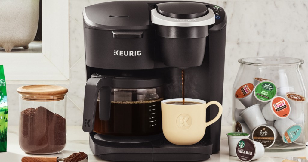 black coffee maker, ground coffee, coffee single serve pods, and cup of coffee on counter