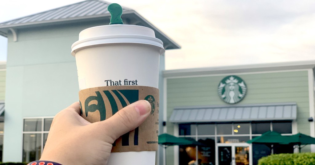 hand holding a cup of pumpkin chai in front of starbucks store