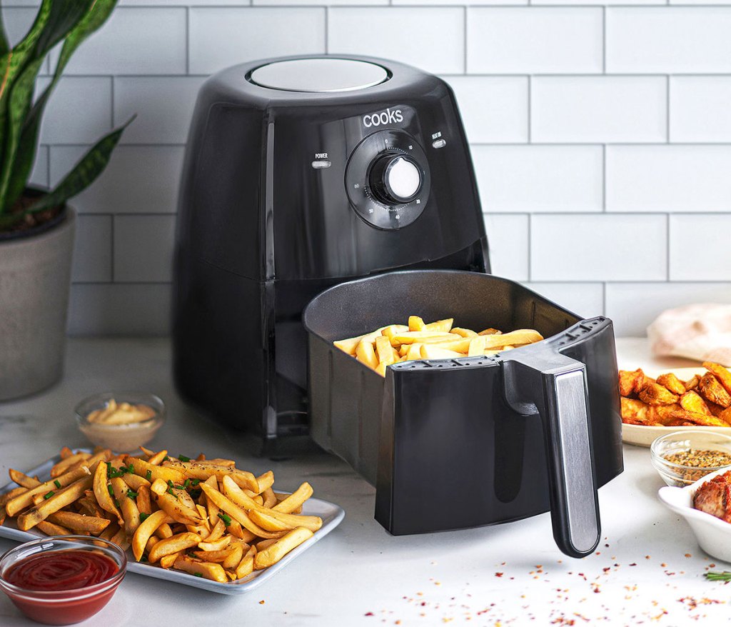 black air fryer on kitchen counter with fries in basket and fried food on plates around it