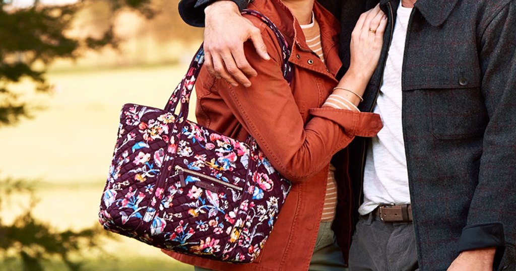 woman in an orange jacket with a deep purple floral print vera bradley tote bag on her shoulder