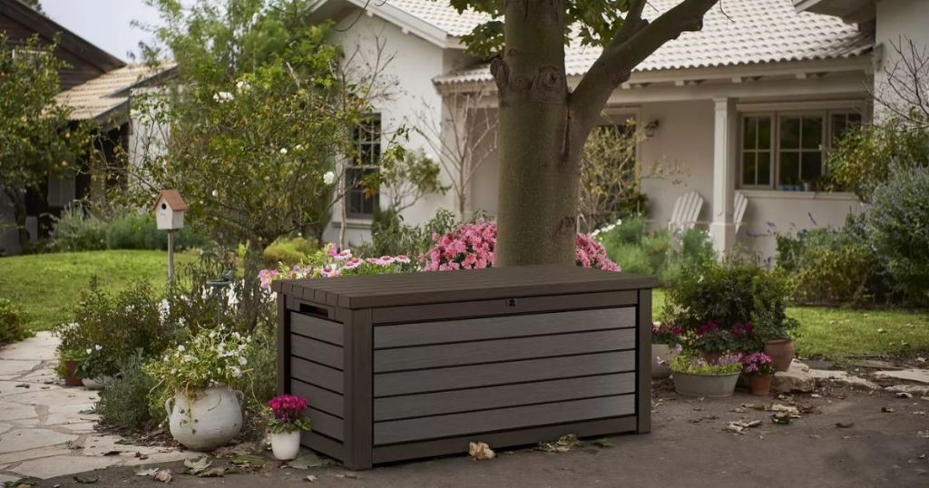 Keter 165 Gallon Outdoor Storage Box outdoors by tree in brown
