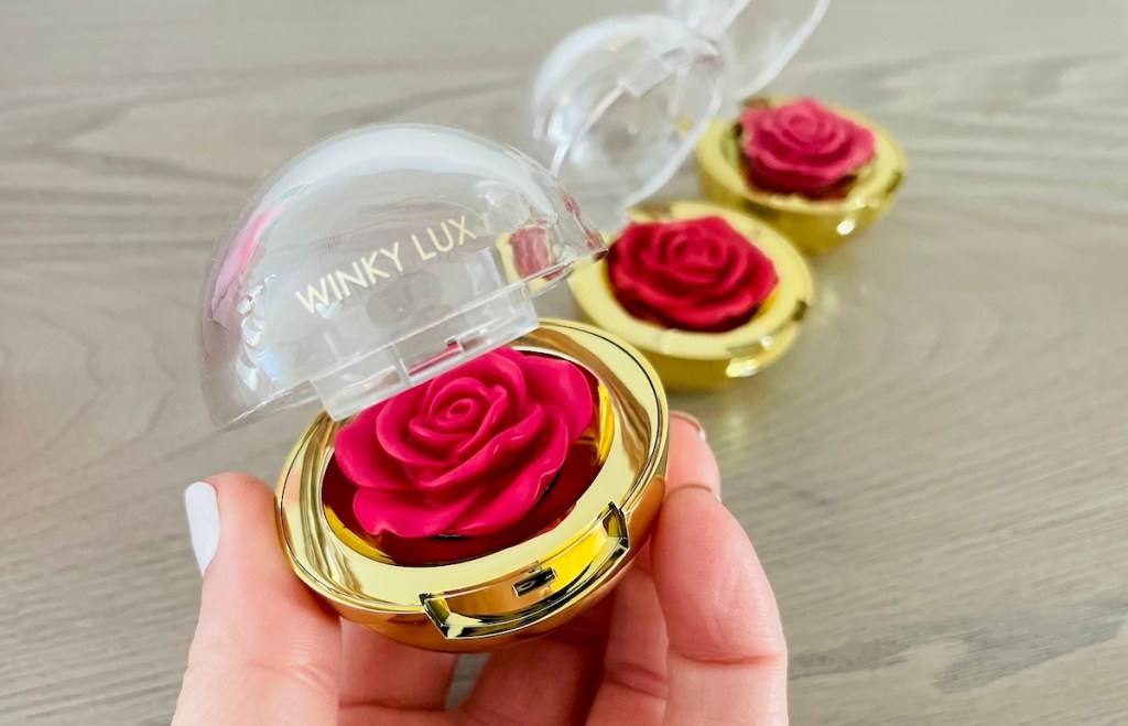 hand holding winky lux cheeky rose blush with other on table in background