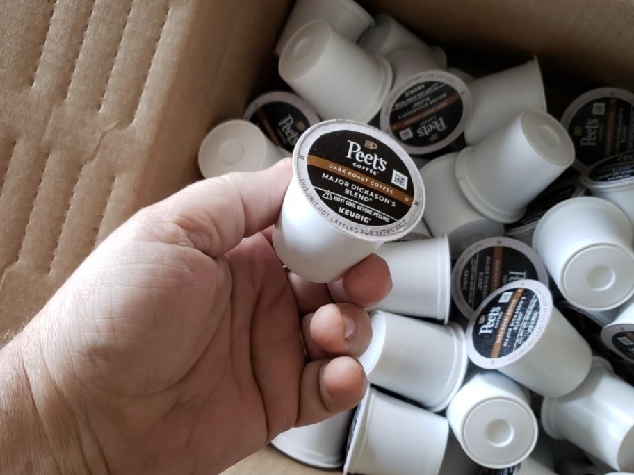 hand holding coffee pod and coffee pods in shipping box