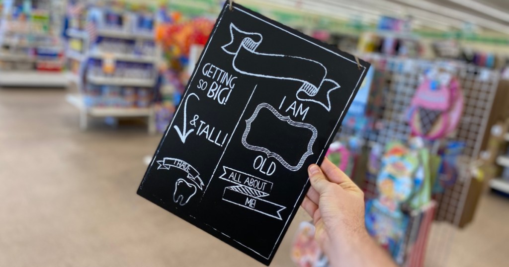 hand holding baby milestone chalk board near in-store display