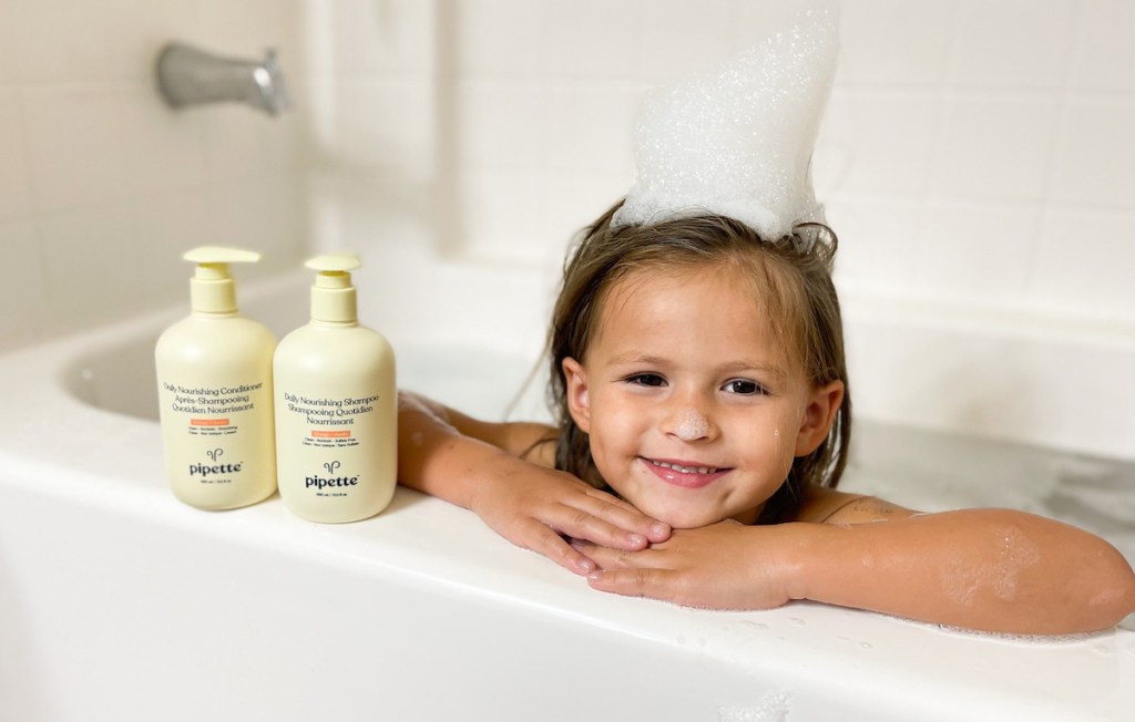 girl with bubbles on head leaning on bathtub edge