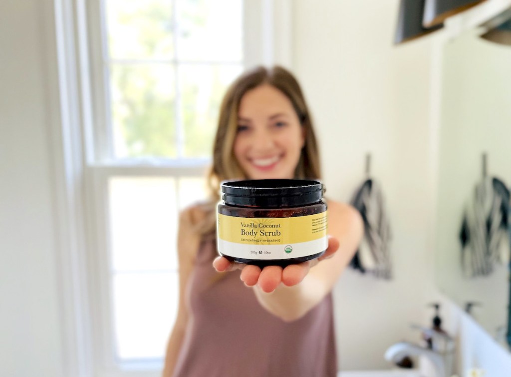 woman holding jar of beauty by earth vanilla coconut body scrub in bathroom