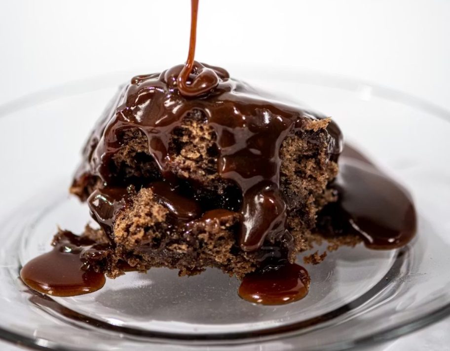 sticky toffee pudding on a plate with sauce being drizzled over it