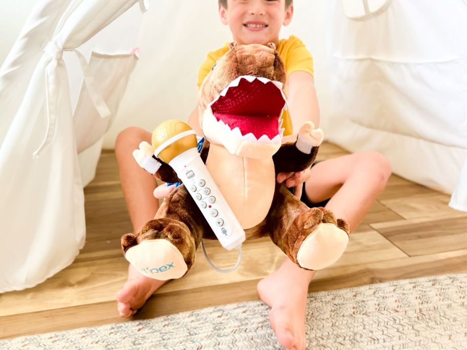 boy holding Sing Along Crew T-Rex under white tent