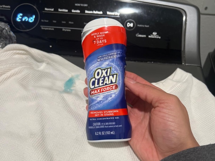 person holding oxiclean stain remover stick in front of shirt on washing machine
