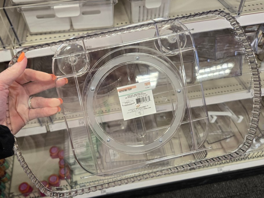 A person with orange nail polish holds a clear, rectangular storage container with multiple compartments. It's displayed on a store shelf.