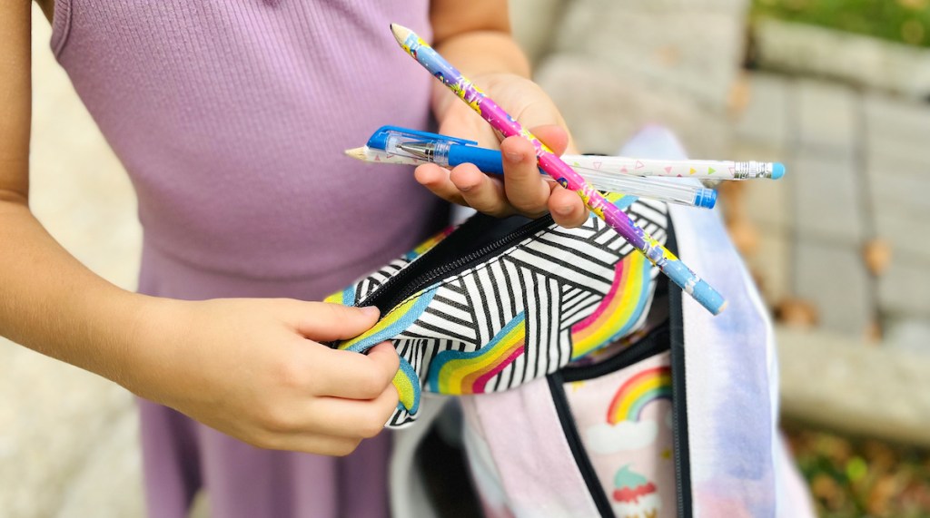 hands taking pens out of rainbow pencil case