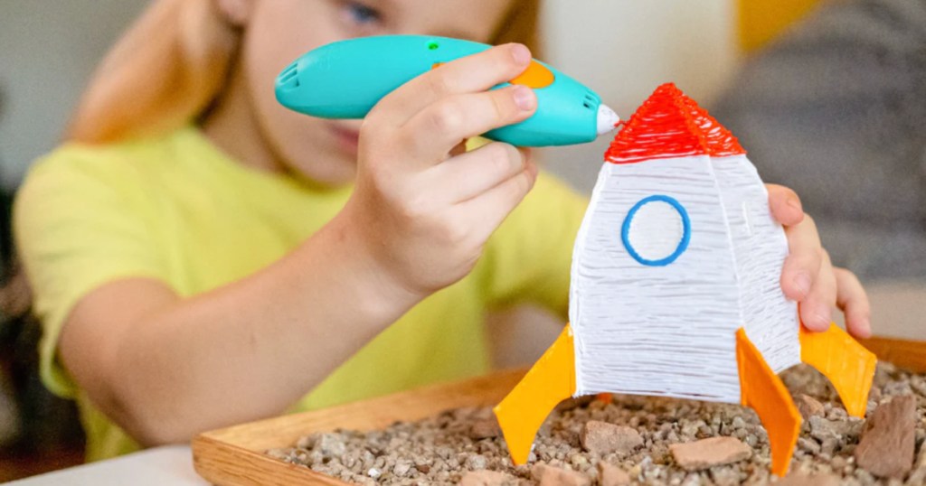 Little girl using 3-D doodler pen to create a rocket ship