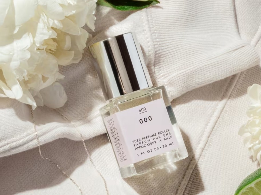 a bottle of perfume oil pm a white cloth next to a white flower