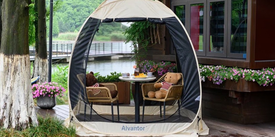 tan and black pop up tent with table, chairs and teddy bear under it 