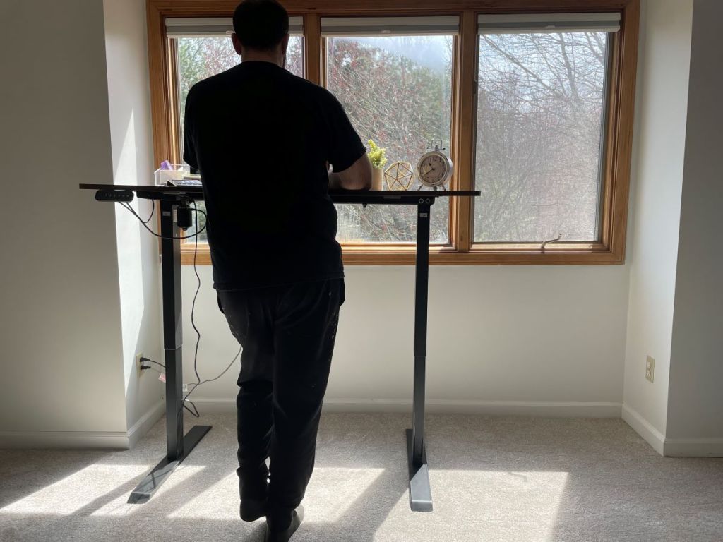 Man standing next to a standing desk placed by a window