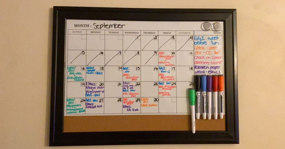 cork bulletin board on wall with writing and markers on it