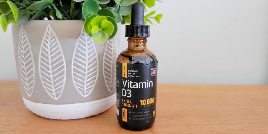 brown glass bottle with black and yellow label that says Raw Science Vitamin D3 next to a plant in a grey and white pot