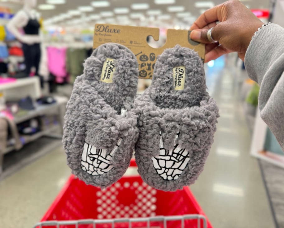 hand holding a pair of dearfoam kids skeleton slippers from