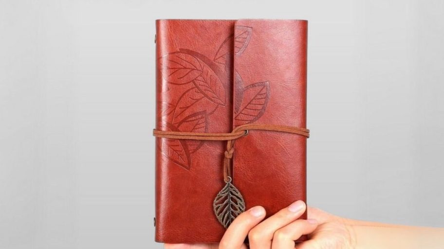 a hand holding a small pu leather bound journal with a leaf motif