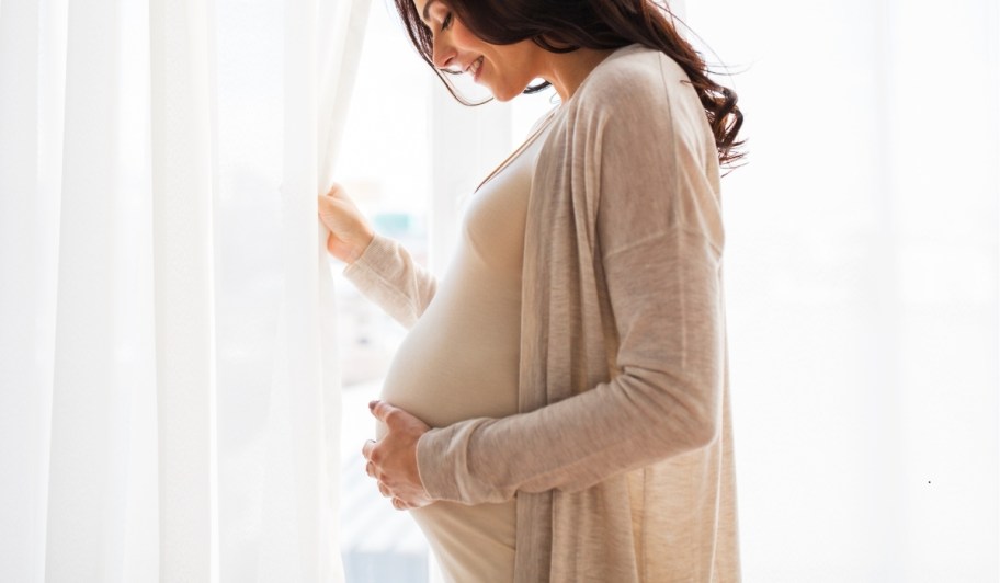 woman holding belly standing in front of widow