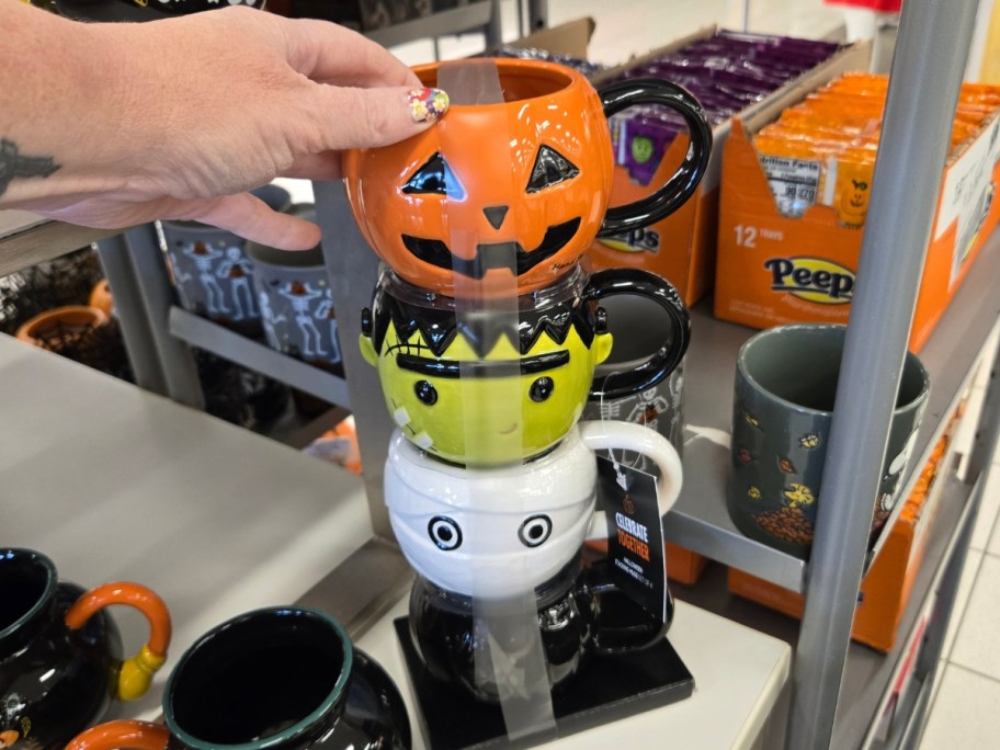 hand reaching for a set of 4 stacking Halloween coffee mugs on a store shelf