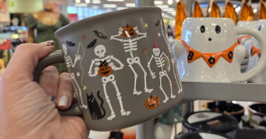 hand holding a coffee mug with dancing skeletons on it