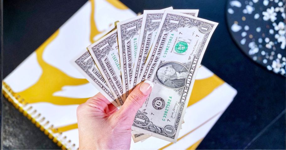 hand holding five one dollar bills