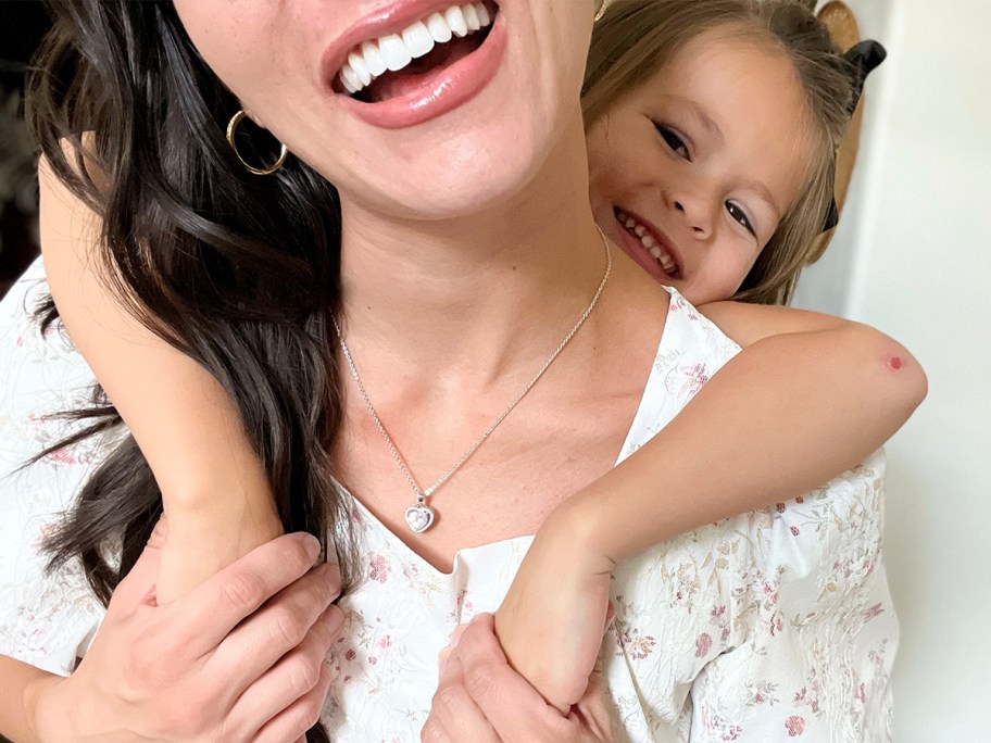 woman wearing white gold heart necklace with child behind her