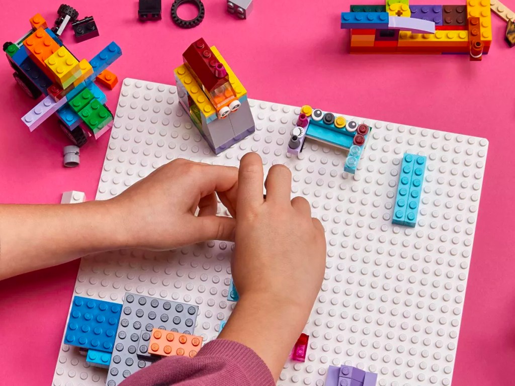 kid adding legos to white lego baseplate