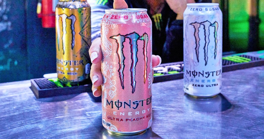 person grabbing a pink can of monster energy drink from desk