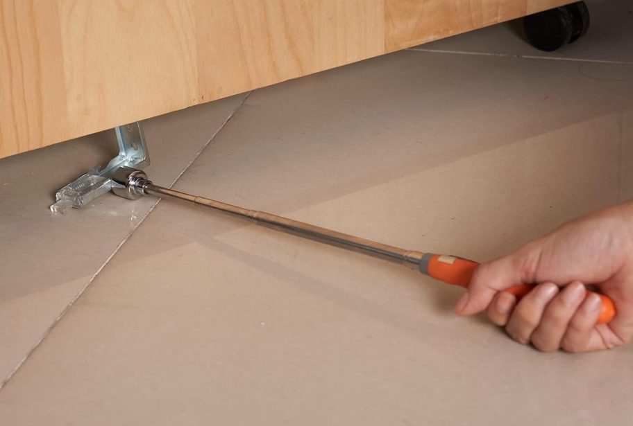 hand holding telescoping magnet tool pulling metal piece from under cabinet