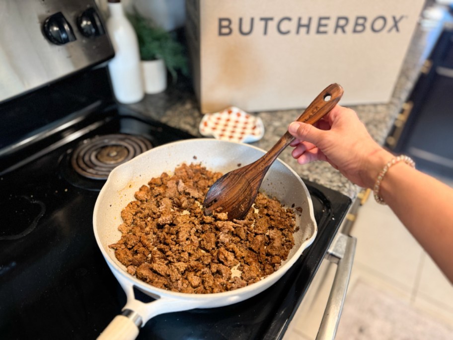 person cooking chicken in a pan with a butcherbox package behind it