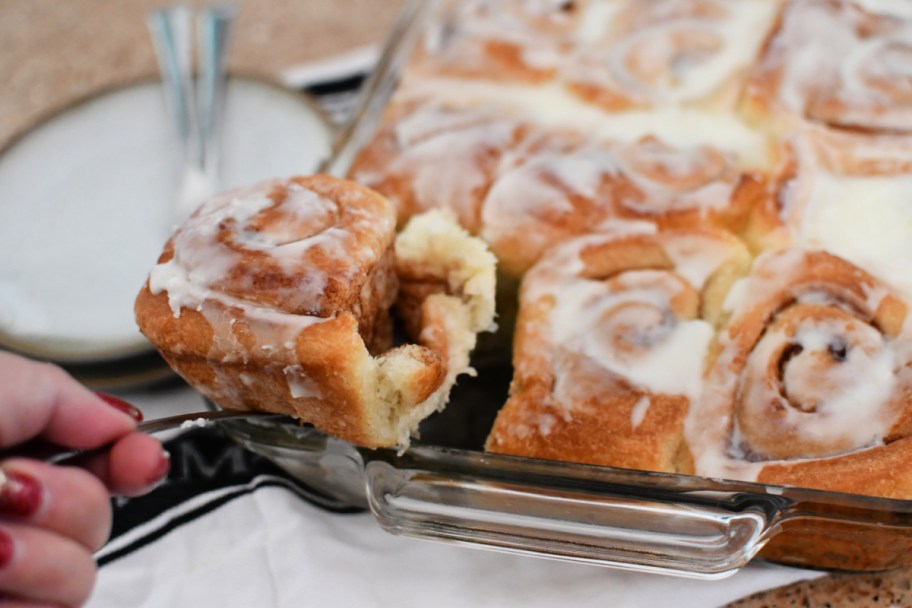 hand lifting a cinnamon roll out of a pan of freshly baked rolls
