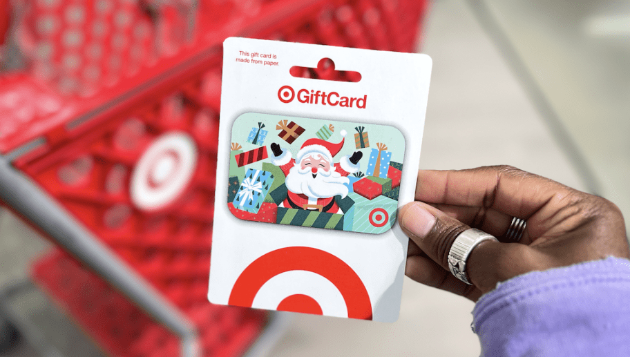 hand holding up target gift card in front of red shopping cart