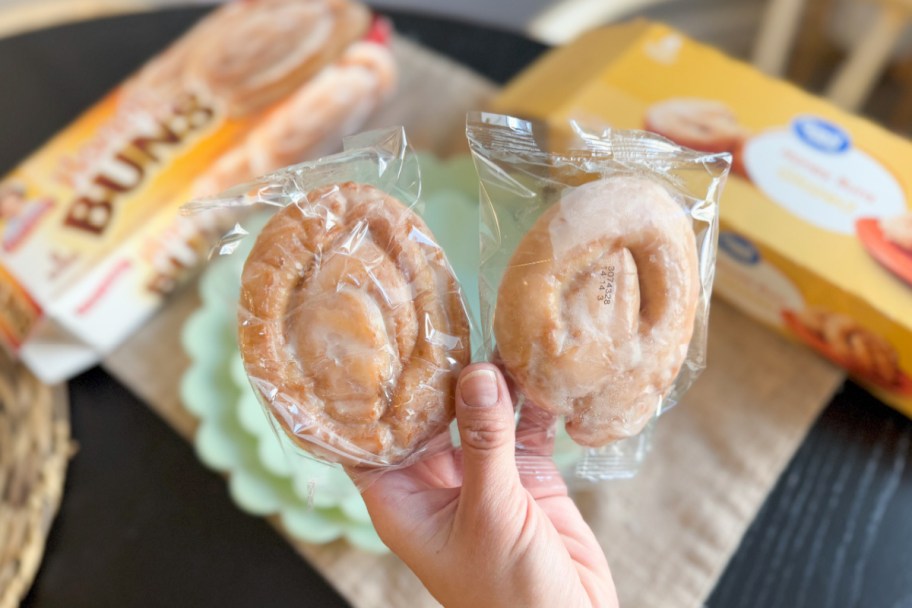 hand holding two cinnamon buns in wrapper