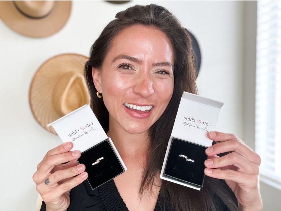 woman holding up 2 pairs of hoop earrings while also wearing hoop earrings